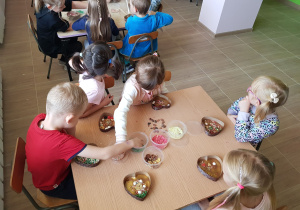 Dzieci siedzą przy stoliku i tworzą swoje czekolady.