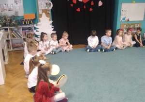 Dzieci siedzą na dywanie, trzymają instrumenty muzyczne