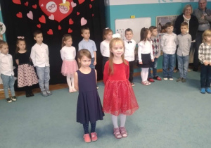 Lucynka i Marysia stoją na środku sali, recytują wiersze dla Babci i Dziadka