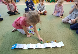 Marysia układa kształty od najmniejszego do największego, pracując z książeczką "Zyk - zag"