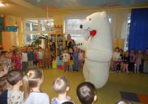 Dzieci stoją w kole a w środku jest duży, biały miś