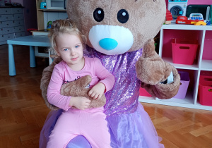 Oliwka pozuje do zdjęcia z misiem ubranym w fioletową spódniczkę i kokardkę