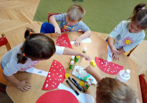 Dzieci palcami umoczonymi w białej farbie tworzą kropki na kapeluszu muchomora