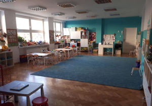 Sala grupy Kotki jest biało-turkusowa. Na górze są lampy a z lewej strony stoją cztery stoliki dziecięce.