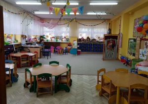 Sala grupy Delfinki jest urządzona w kolorystyce niebieskiej i żółtej. Na górze znajduja się lapmy, na których powieszone są dekoracje wiosenne. Na końcu sali są kolorowe regały z zabawkami dla dzieci.