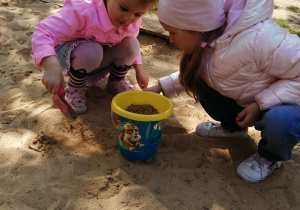 Oleksandra i Victoria robią babkę z piasku.