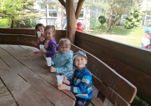Dzieci jedzą w altanie zrobioną sałatkę owocową w kubeczkach