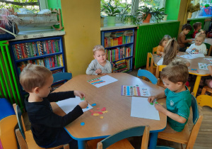 Dzieci przy niebieskim stoliku wypychają z kartki kolorowe kropki