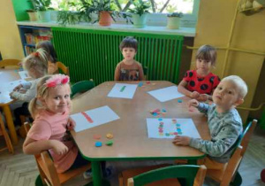 Dzieci przy zielonym stoliku tworzą kreatywne kompozycje z kolorowych kropek