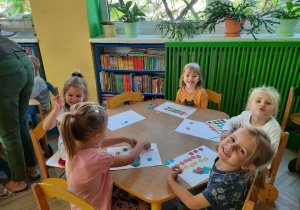 Dzieci przy żółtym stoliku tworzą kreatywne kompozycje z kolorowych kropek