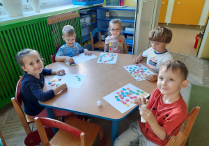 Dzieci przy niebieskim stoliku tworzą kreatywne kompozycje z kolorowych kropek