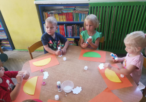 Dzieci przy żółtym stoliku tworzą pracę plastyczną "Bajkowy samochód"