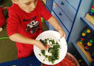 Jasio wsypuje pokrojoną bazylię do garnka z pomidorami i czosnkiem