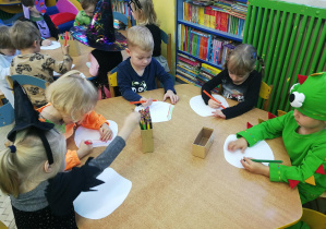 Dzieci przy żółtym stoliku kolorują sylwety fartuszków