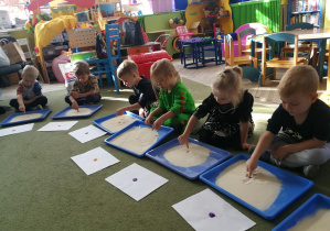 Dzieci tworzą wzory kropek/plamek na tackach z kaszą manną w rytmie piosenki "Ja i ty"