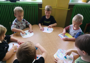 Dzieci przy zielonym stoliku odtwarzają palcami umoczonymi w farbie rytm piosenki "Ja i ty", tworząc kropki