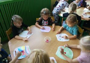 Dzieci przy żółtym stoliku odtwarzają palcami umoczonymi w farbie rytm piosenki "Ja i ty", tworząc kropki