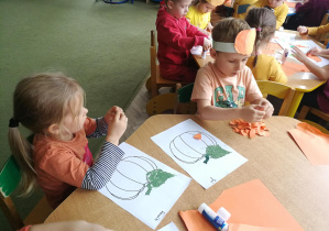 Jasio i Remik naklejają kawałki pomarańczowej kartki na sylwety swoich dyń
