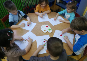 Przedszkolaki wystukują rytm piosenki "Kolorowe światła", tworząc kropki z farby na kartach z sygnalizatorami