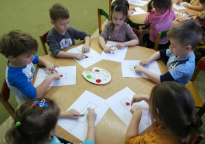 Przedszkolaki tworzą kropki z farby na kartach z sygnalizatorami, rytmizując piosenkę "Kolorowe światła"