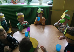 Dzieci przy zielonym stoliku próbują gruszki i kompot