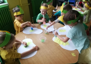 Dzieci przy zielonym stole stemplują pędzlami z gąbek umoczonymi w farbach sylwety gruszek
