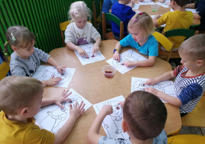 Dzieci przy żółtym stoliku wystukują rytm piosenki "Oczy Jesieni" na ilustracjach palcami umoczonymi w farbach - dwie kropki w ustawieniu poziomym