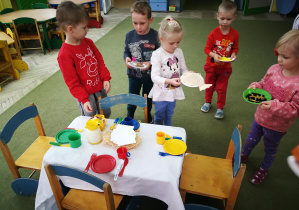 Dzieci ustawiają potrawy na wigilijnym stole dla misiów i lalek