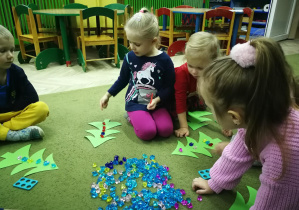 Dzieci układają diamenciki na sylwetach choinek