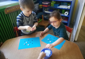 Oliwka i Mateusz wyklejają wzór kulkami z białej bibuły