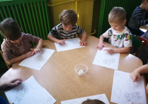 Dzieci przy zielonym stoliku stemplują rytmicznie wzór farbą, śpiewając piosenkę "Tak się zachmurzyło"