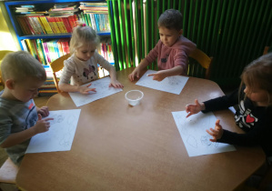 Dzieci przy żółtym stoliku stemplują rytmicznie wzór farbą, śpiewając piosenkę "Tak się zachmurzyło"