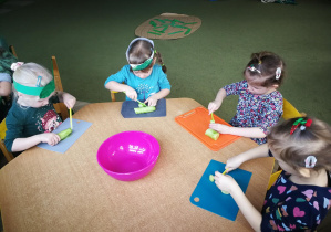 Dzieci przy żółtym stoliku kroją ogórki w plasterki