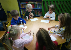 Dzieci przy żółtym stoliku wyklejają wzór - kropki w ustawieniu koła