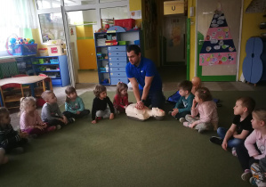 Ratownik medyczny pokazuje dzieciom w jaki sposób wykonać masaż serca