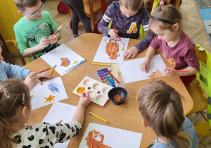 Dzieci przy żółtym stoliku malują farbami bohatera ksiązki