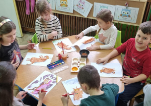 Dzieci przy niebieski, stoliku malują farbami bohatera książki