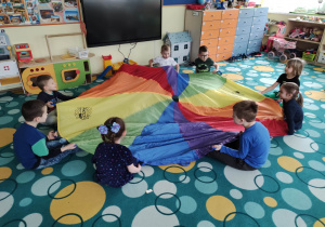 Dzieci bawią się na dywanie z wykorzystaniem chusty animacyjnej