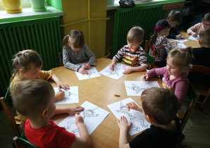 Dzieci przy zielonym stoliku rysują kredką pastelową dwie pionowe linie do piosenki "Pajacyk"