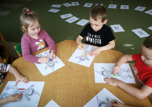 Oliwia, Jasio i Tymek rysują kredką pastelową dwie pionowe linie do piosenki "Pajacyk"