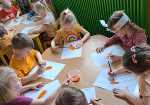 Przedszkolaki malują pomarańczową farbą sylwety marchewek