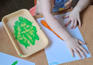 Hania S. odciska na kartce dłoń umoczoną w zielonej farbie, tworząc liście marchewki