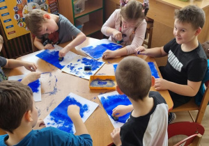 Dzieci wykonują tło do swojej pracy plastycznej