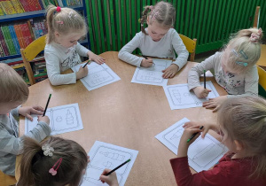 Dzieci przy żółtym stoliku rysują ołówkiem na rysunkach poziome linie od lewej do prawej w rytmie piosenki "Zaczarowany ołówek"