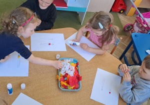Dzieci przy niebieskim stoliku wyklejają wzory kulkami bibuły - dwie równoległe linie ułożone w poziomie