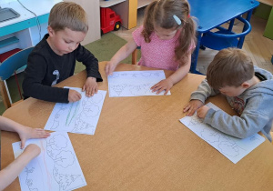 Dzieci przy niebieskim stoliku odtwarzają graficznie wzór dwóch poziomych linii