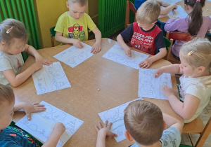 Dzieci przy zielonym stoliku odtwarzają graficznie wzór dwóch poziomych linii