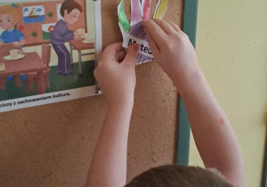Mateusz przyczepia papierową dłoń na tablicy z zasadami przedszkolnymi Puchatków