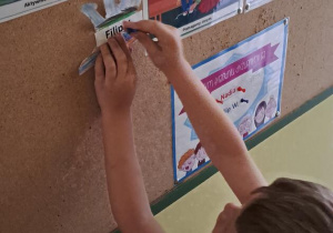 Filip przyczepia papierową dłoń na tablicy z zasadami przedszkolnymi Puchatków