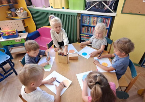 Dzieci przy żółtym stoliku tworzą z kropek kolorowe prace
